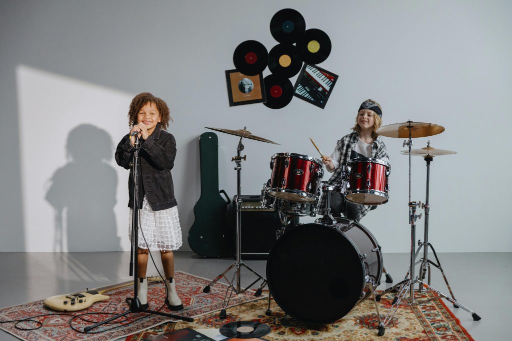Children singing and drumming joyfully in a music studio with instruments.